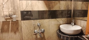 Un baño con pared de mármol, lavamanos y ducha.