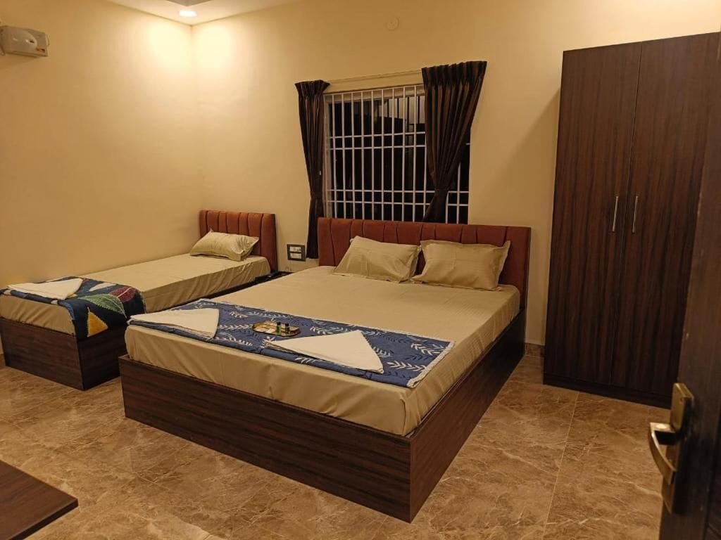 A hotel room with two beds, a wardrobe, a window with curtains, and a bedside table.