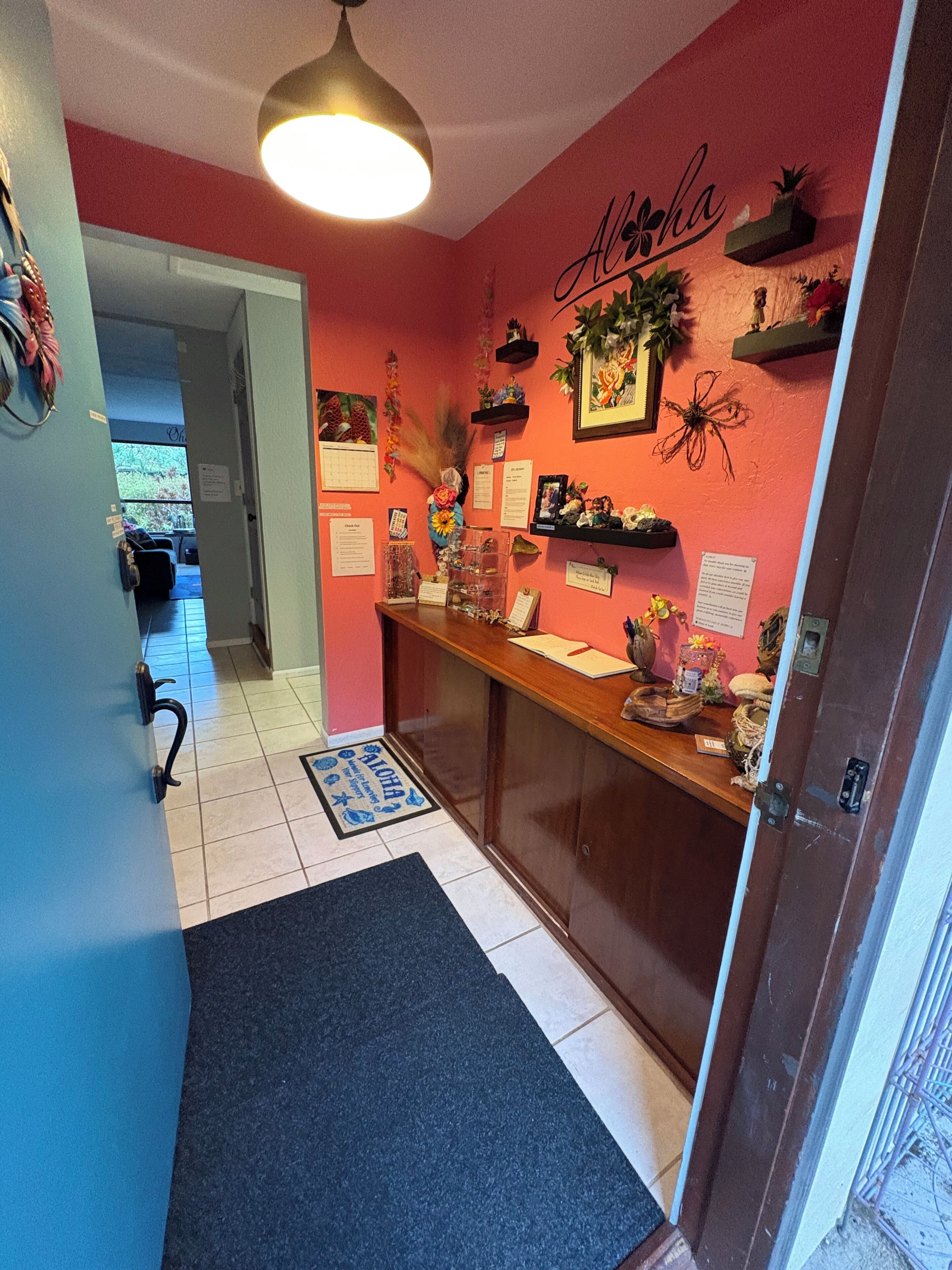 Un pasillo con un mostrador de recepción de madera, un tapete negro y una pared roja decorada con diversos adornos.