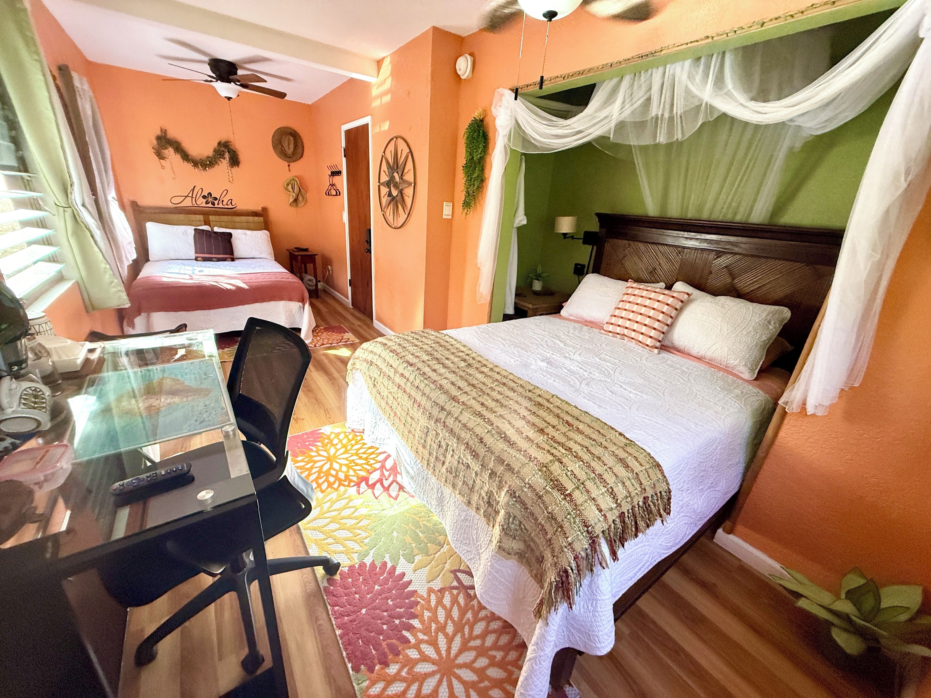 Un dormitorio con cama, escritorio con silla, ventilador de techo y ventana con cortinas.
