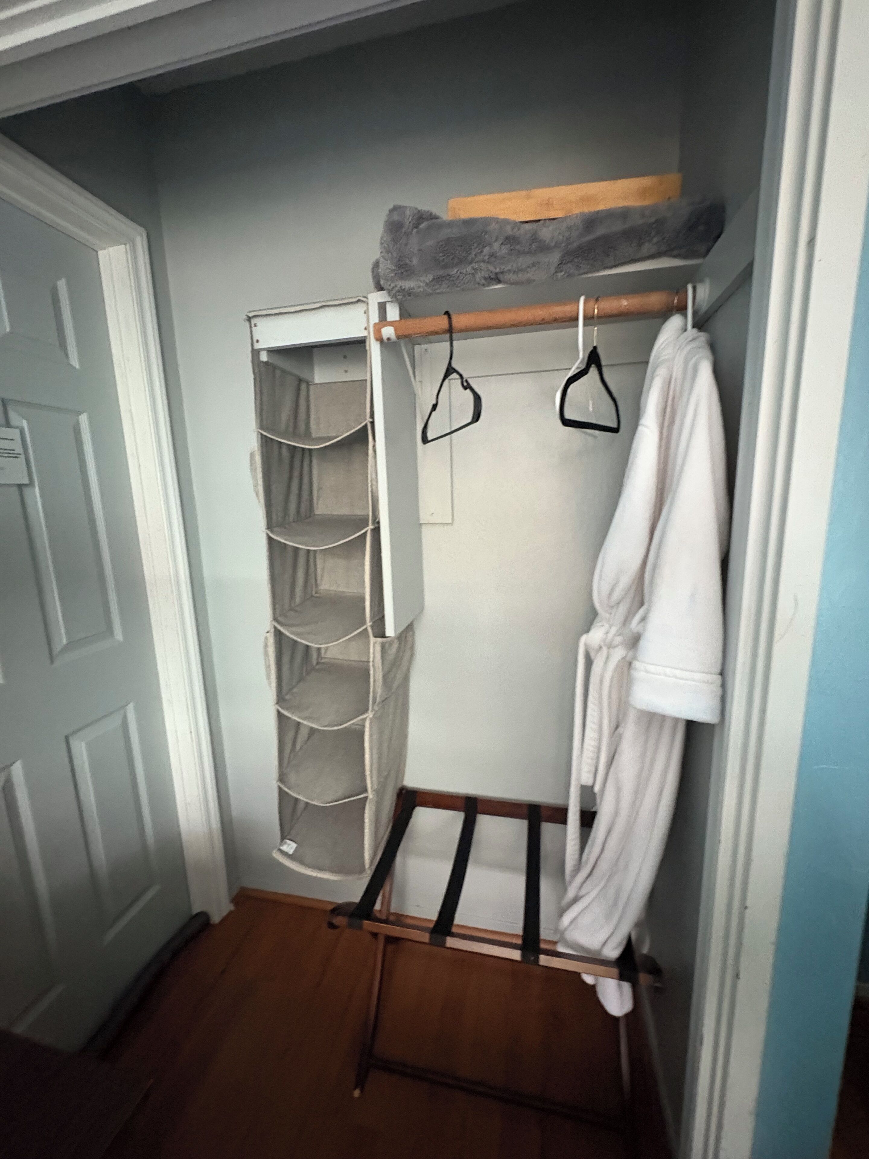 A walk-in closet with a wooden rack, a hanging robe, and a grey storage unit.