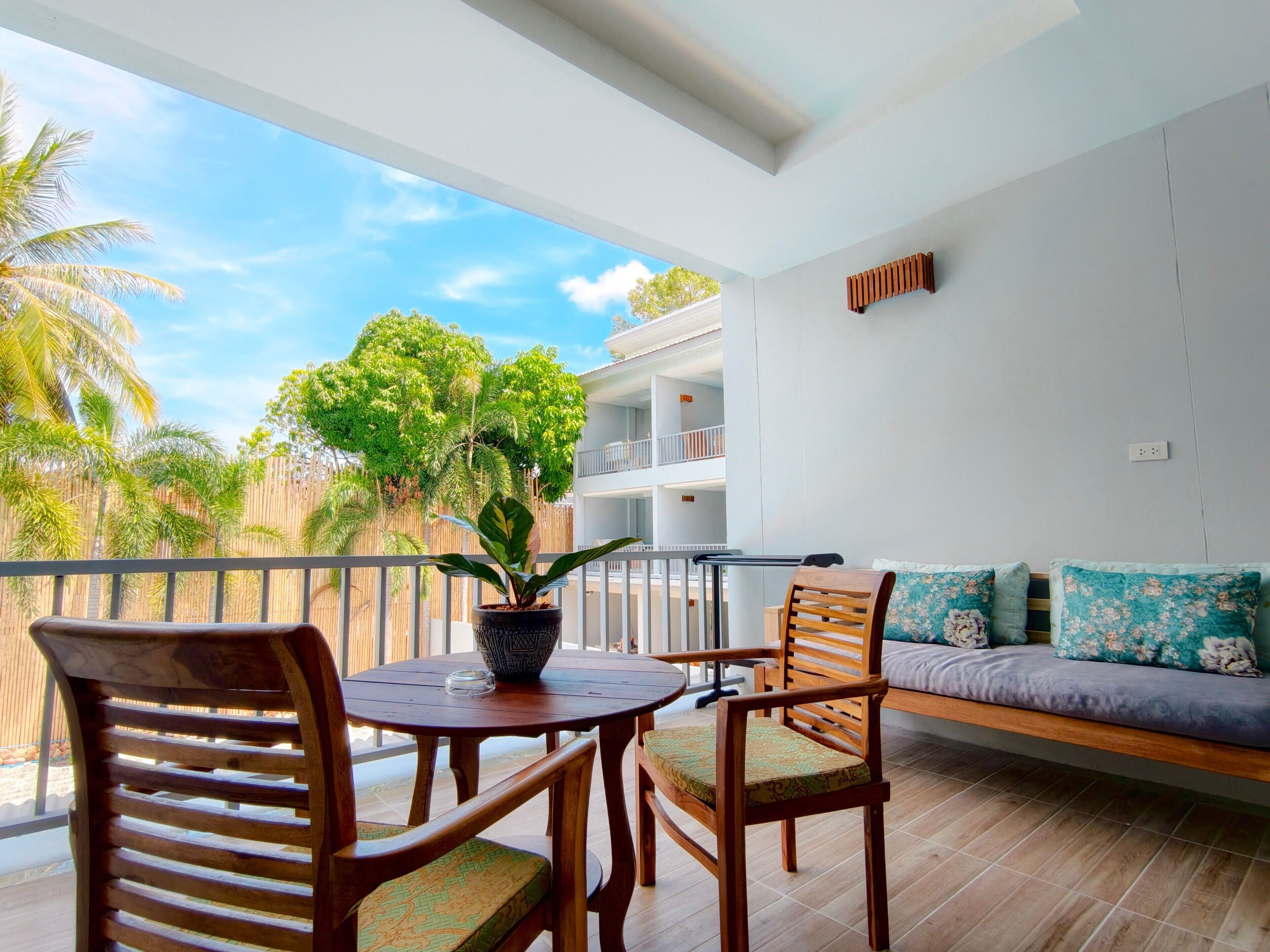 A balcony with a wooden table, chairs, a potted plant, and a sofa with floral cushions.