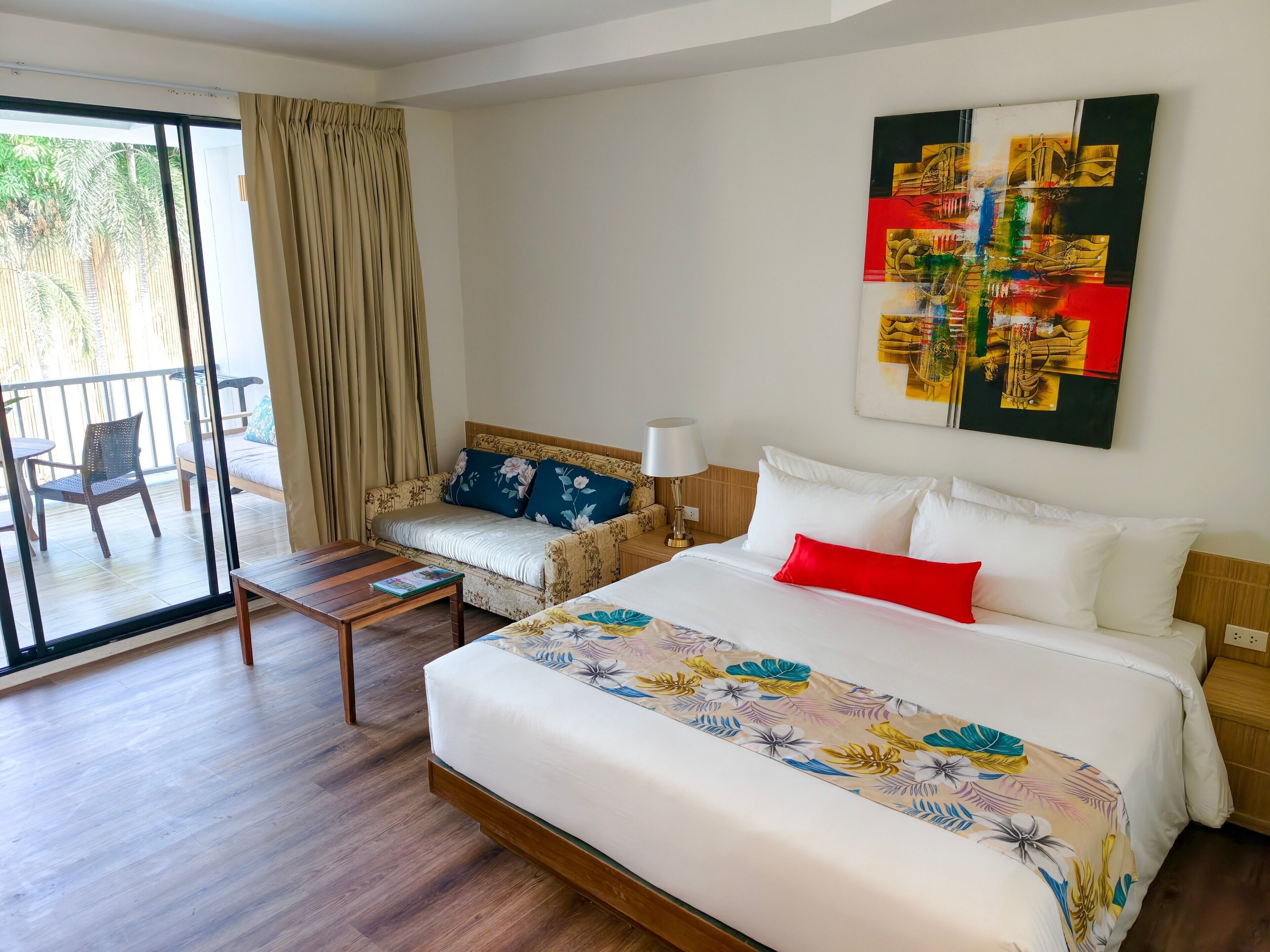 A hotel room with a bed, a sofa, a small table, a lamp, and a view of the outdoors.