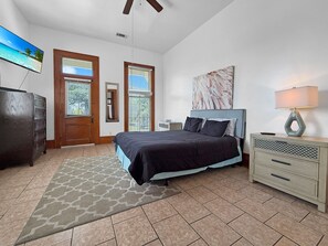 A bedroom with a bed, a nightstand, a lamp, a dresser, a painting, and a television on the wall. - St. Claude Retreat 2BR (New Orleans)