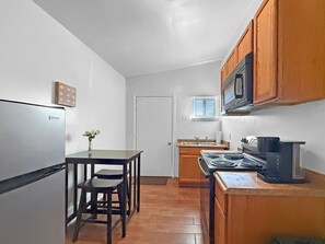 A compact kitchen with a refrigerator, stove, microwave, and wooden cabinets. - St. Claude Retreat 2BR (New Orleans)
