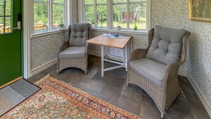 Ein Eckzimmer mit Korbmöbeln, einem kleinen Tisch und Blick ins Freie durch große Fenster.