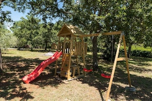 A wooden play structure with a slide and swings in a park. - Villa Fontane (100521-K1) - Funtana (Porec) (Funtana (Porec))