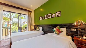 A hotel room with two beds, a green wall, and a balcony with a view of buildings and trees. - Cedar Boutique Hoi An (Da Nang)