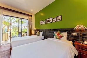 Una camera d'albergo con due letti, una parete verde e un balcone con vista su edifici e alberi.