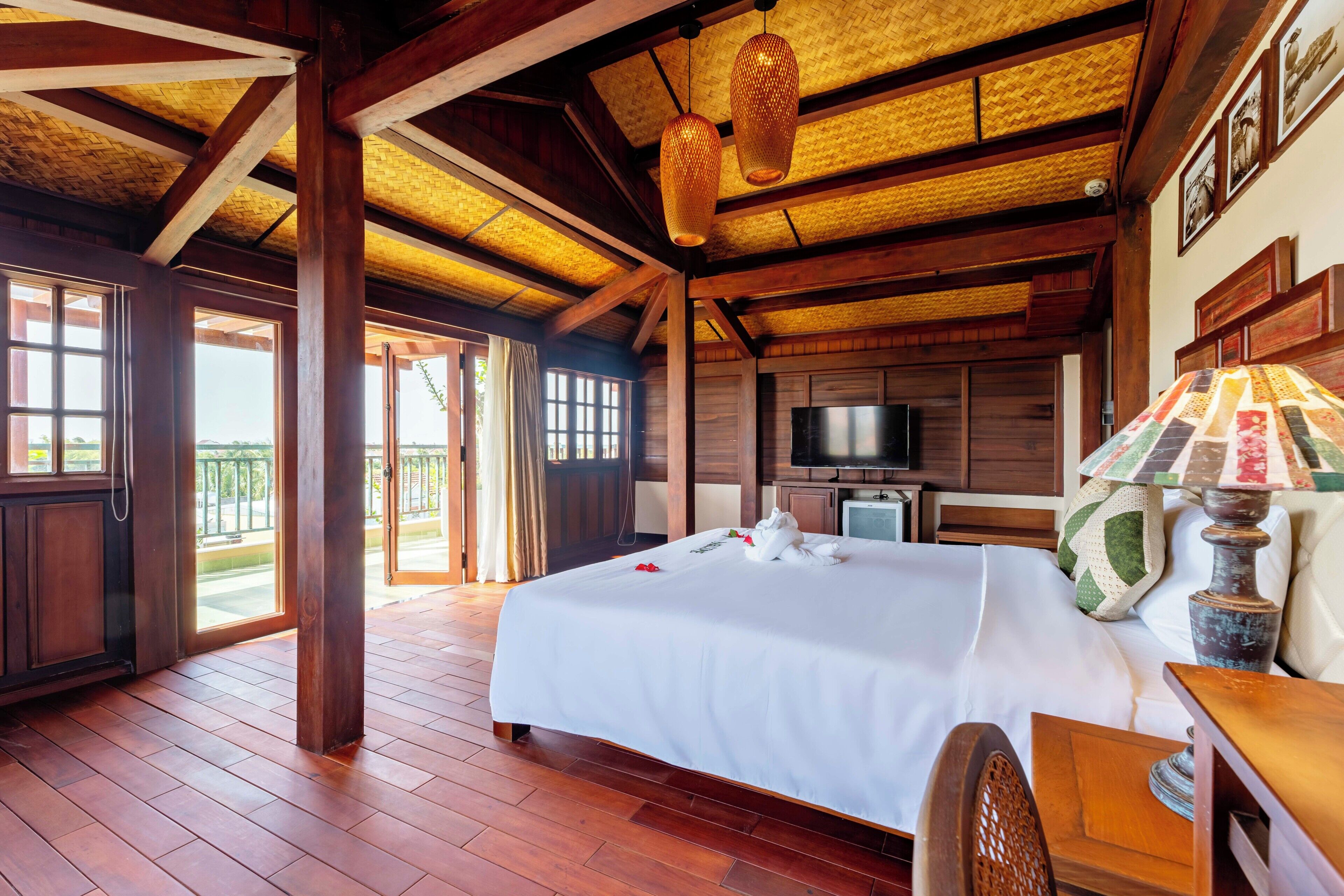 Habitación de hotel con una cama grande, suelo de madera, televisión y balcón con vistas.