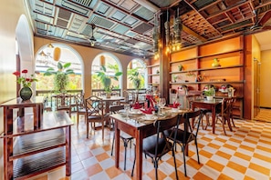 Un ristorante con pavimento a scacchi, arredi in legno e finestre ad arco che si affacciano su un giardino.