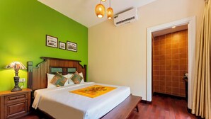 A hotel room with a bed, bedside table, lamp, air conditioning unit, and a wooden door. - Cedar Boutique Hoi An (Da Nang)