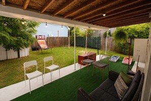 An outdoor patio with artificial grass, a wooden ceiling, and a seating area with chairs and a sofa. - Modern 3BR Houston Home Near Downtown w/ Patio (Houston)