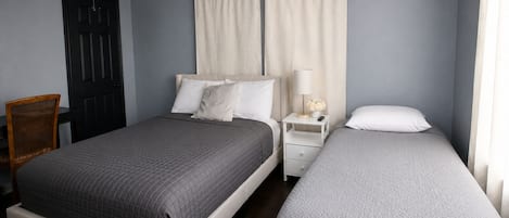 Ein Schlafzimmer mit zwei Betten, einem Nachttisch, einem Sessel und einer Tür.