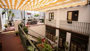 A courtyard with a striped awning, outdoor furniture, potted plants, and a staircase leading to an upper level.