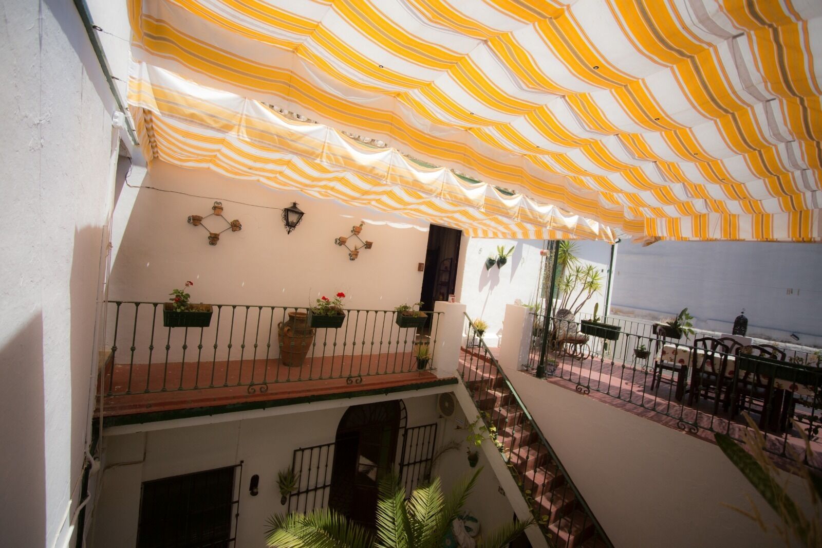 A covered outdoor area with a striped awning, a balcony with railings, potted plants, and outdoor seating.