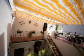 Un espacio al aire libre techado con un toldo a rayas, un balcón con barandillas, plantas en macetas y asientos exteriores.