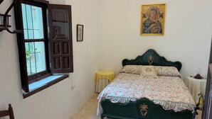 A bedroom with a bed, a window with a view, a wall-mounted picture, and a bedside table.