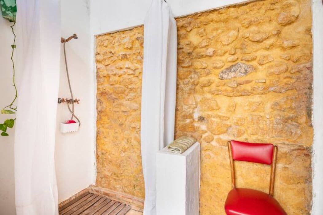 Una habitación con pared de piedra, una silla roja, un radiador blanco y una cortina blanca.