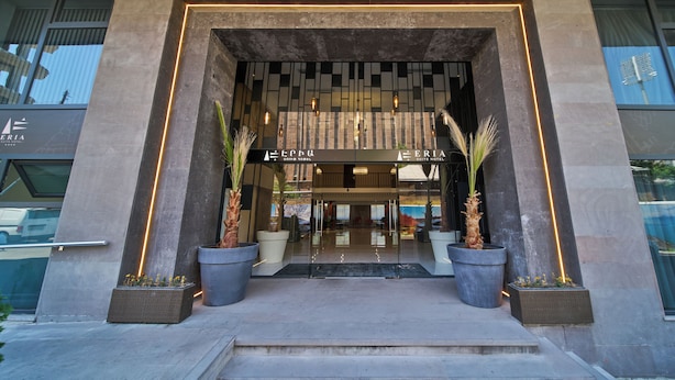 L’entrée d’un hôtel au design moderne, caractérisée par une façade en verre, un espace d’accueil et des plantes en pot.