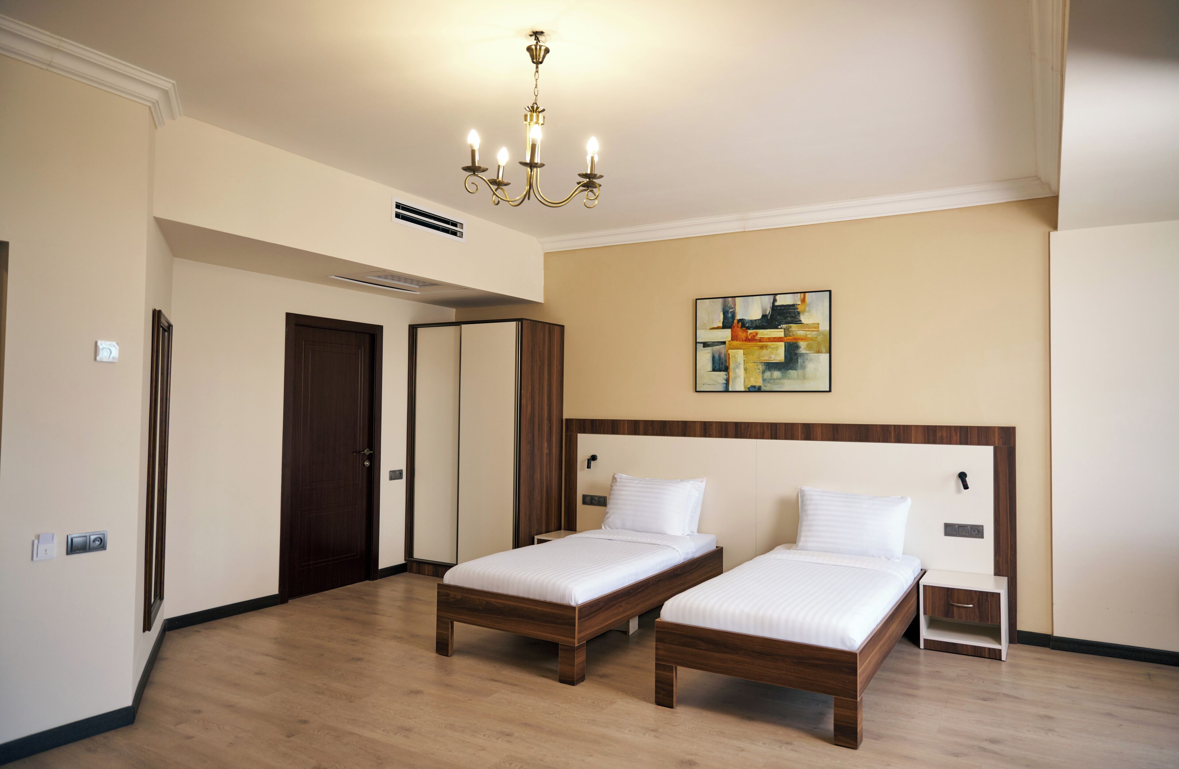 Una habitación de hotel con dos camas individuales, una lámpara en el techo, un cuadro en la pared y una puerta.