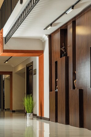A modern lobby with a polished floor, a staircase with a metal railing, and a reception desk with a wooden finish.