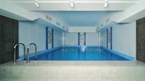 Une grande piscine intérieure à l’eau d’un bleu limpide, entourée de murs recouverts de carreaux bleu clair et de carreaux gris foncé.