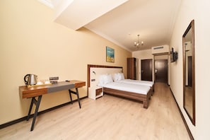 A hotel room with a bed, a desk, a chair, a coffee maker, and a painting on the wall. - Eria Suite Hotel (Yerevan)