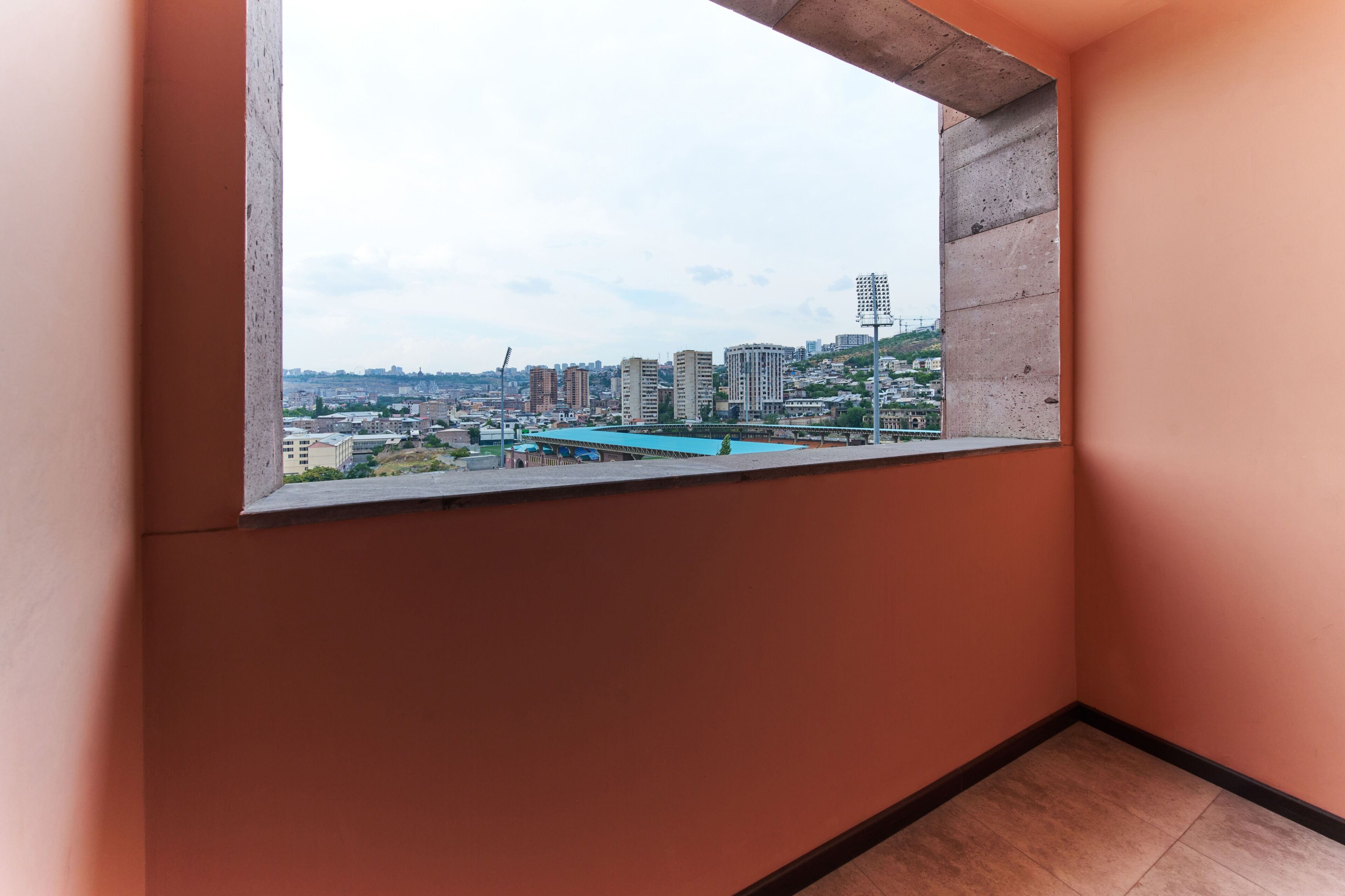 A room with a concrete window sill, a view of a cityscape with buildings and a bridge, and a tiled floor.