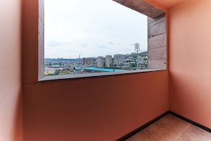 Una habitación con alféizar de hormigón, vistas a un paisaje urbano que incluye edificios y un puente, y suelo de baldosas.