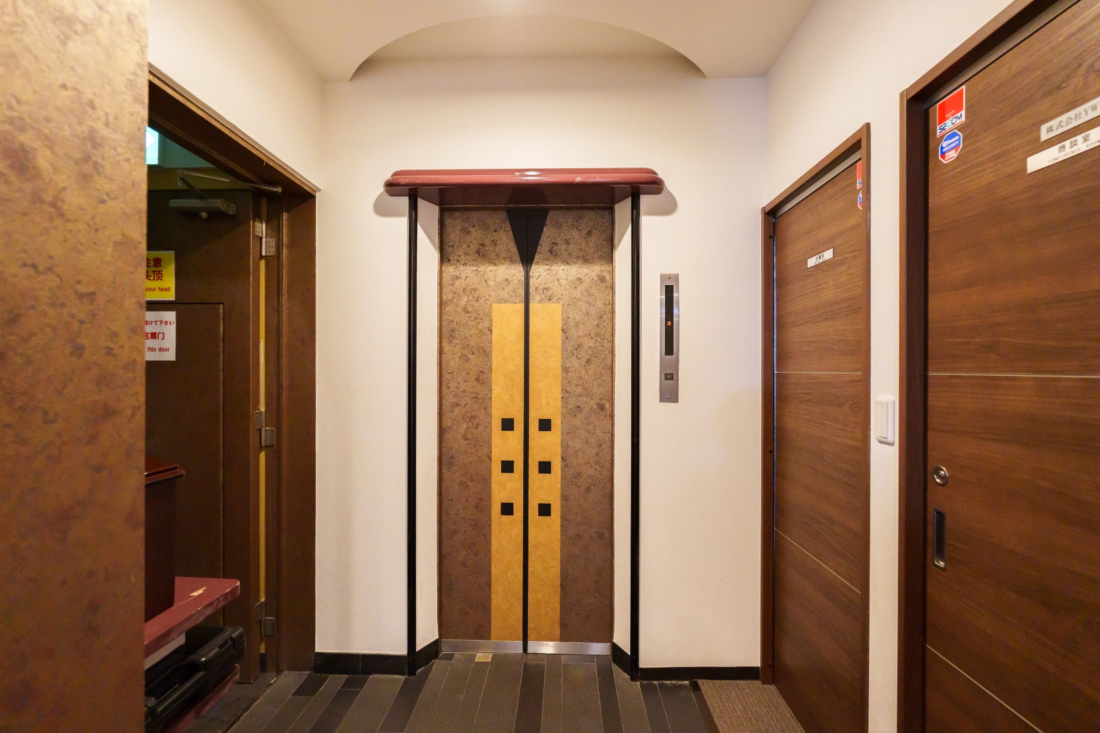 Un ascenseur orné d’une bande jaune et de carrés noirs, flanqué de portes en bois avec une enseigne au-dessus.