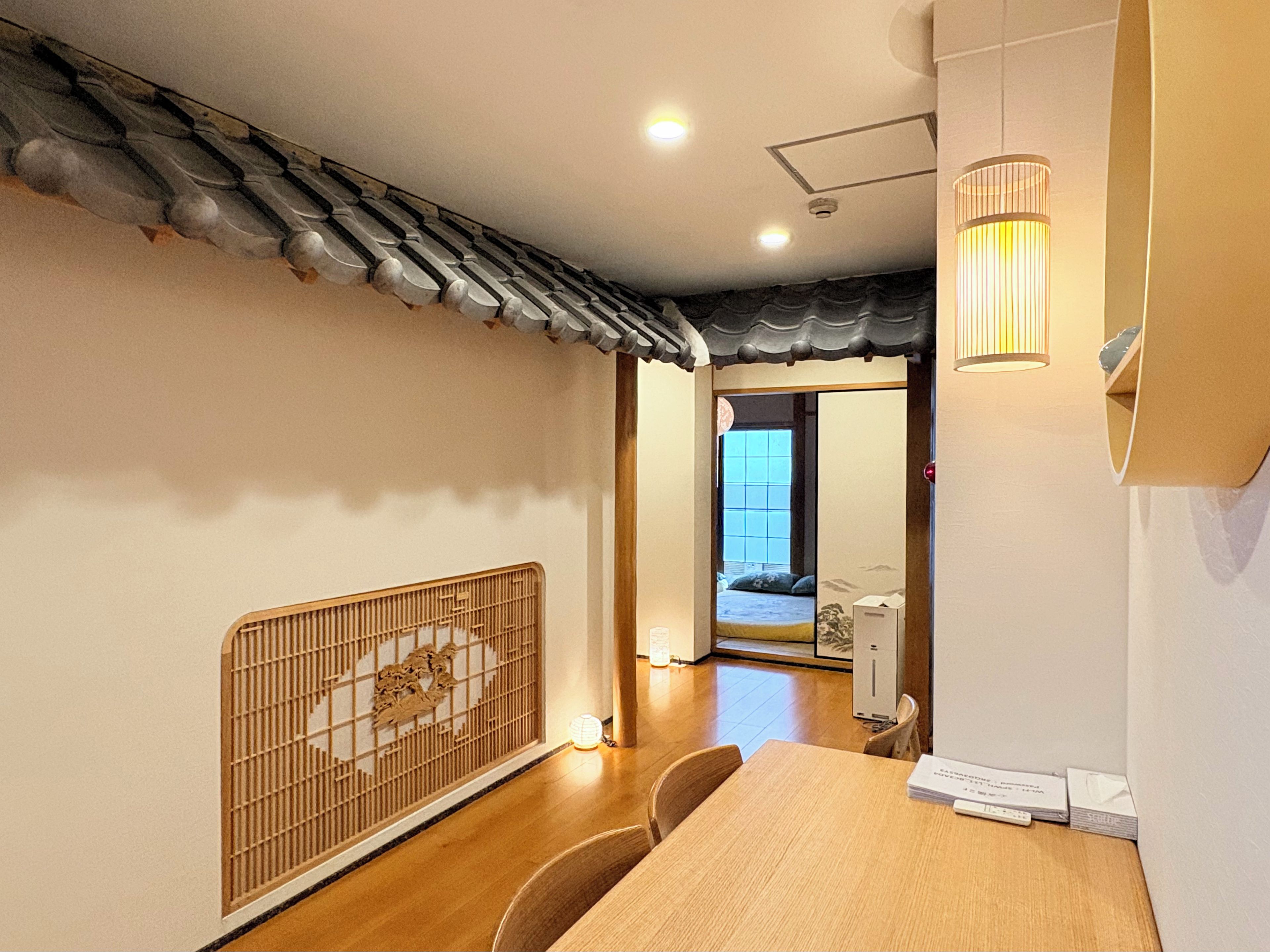 Une pièce de style japonais traditionnel, avec un sol recouvert de tatamis, un paravent shoji, une petite table en bois et une porte coulissante donnant sur une chambre.