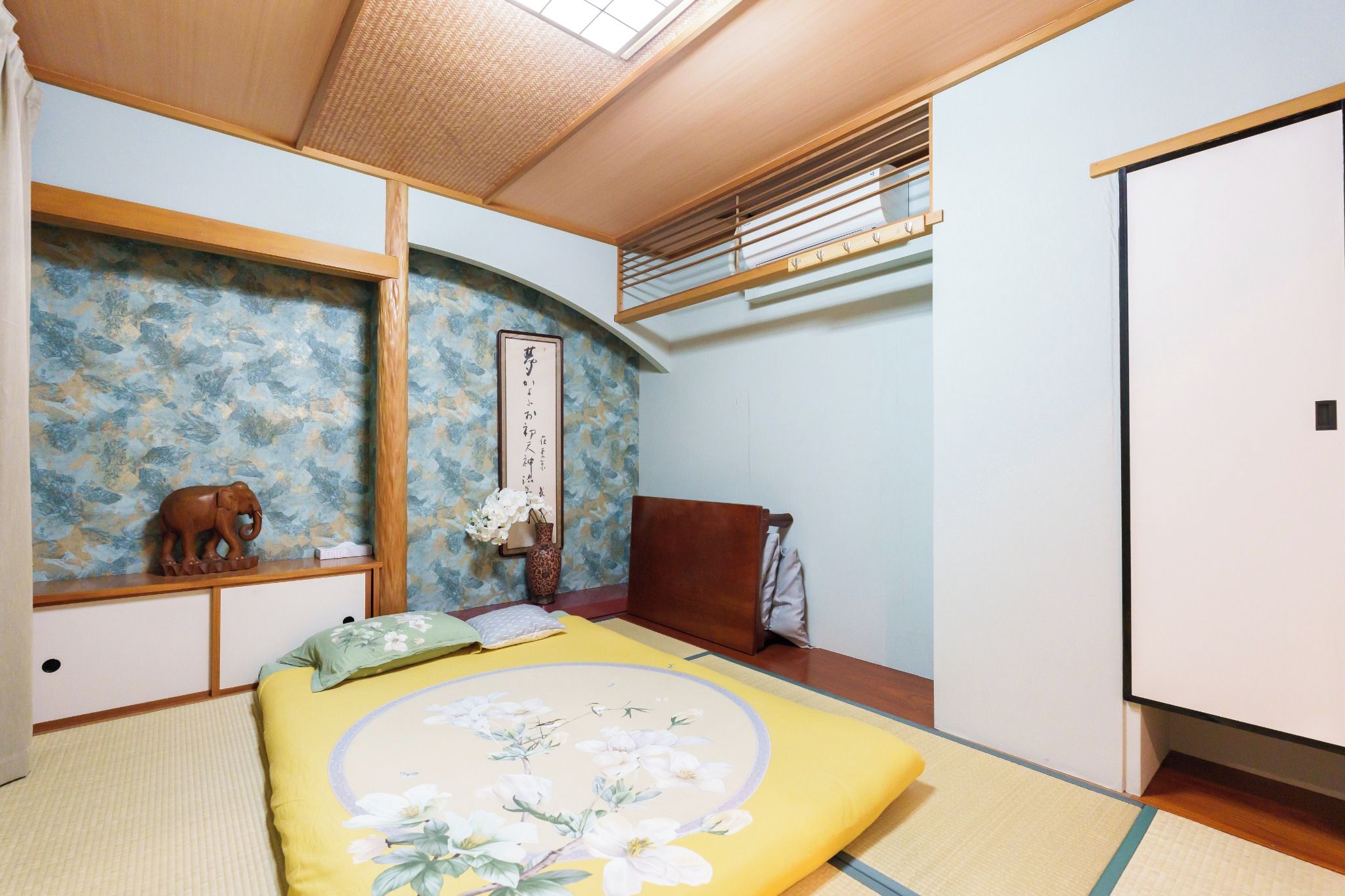 A traditional Japanese-style bedroom with tatami flooring, a futon bed, a shoji screen, and a sliding door.