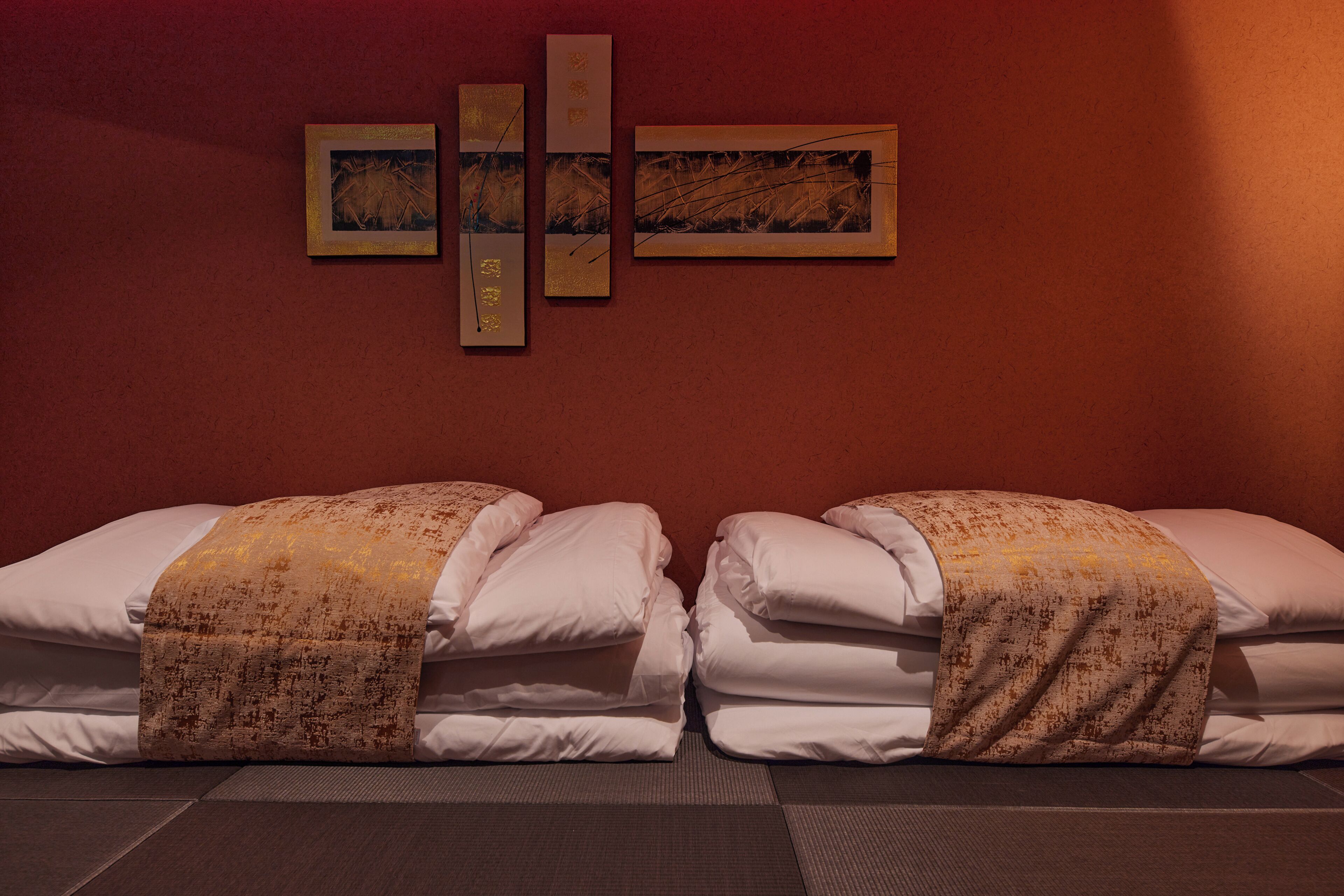 A hotel room with two beds, a red wall, and three framed artworks.