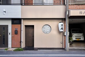 Eine Gebäudefassade mit einer Holztür, einem Rundfenster und einem weißen Laternenleuchter mit japanischen Schriftzeichen.