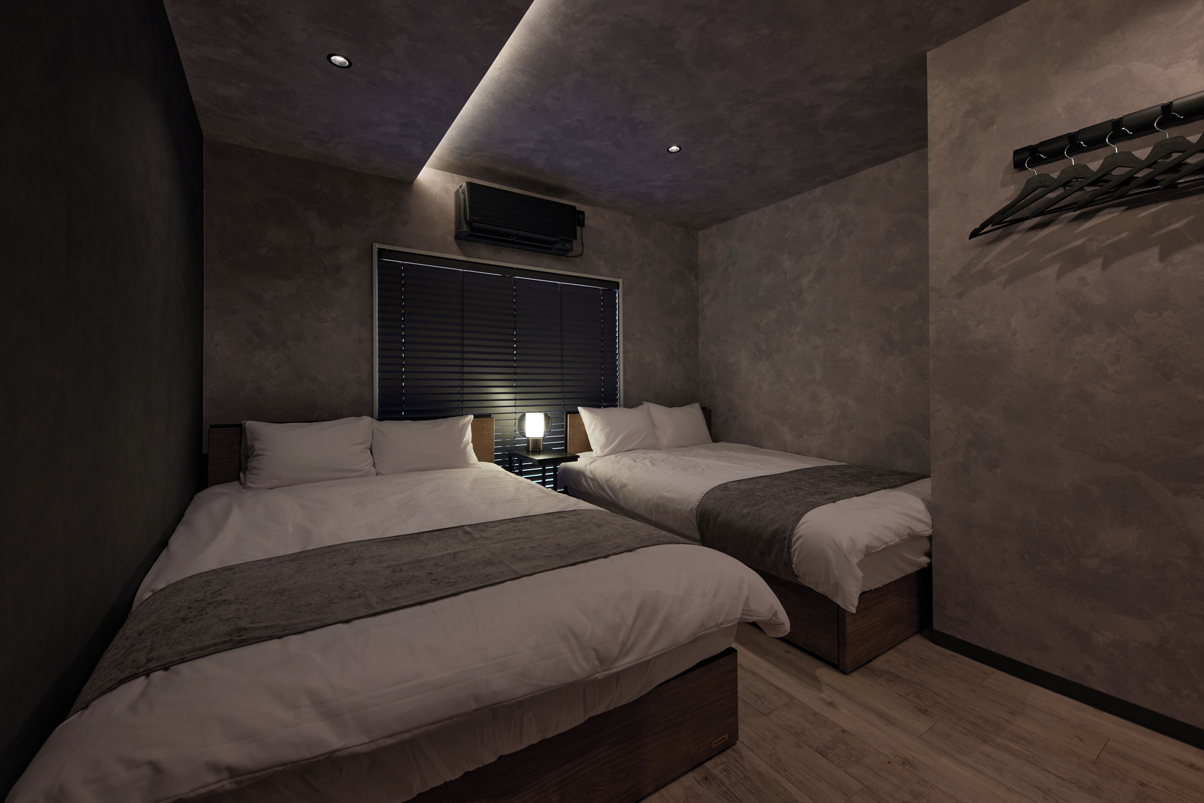 A modern bedroom with two beds, a ceiling light, and a wall-mounted air conditioning unit.