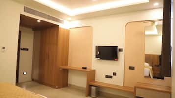 A hotel room with a bed, a TV mounted on the wall, a wooden wardrobe, and a mirror.