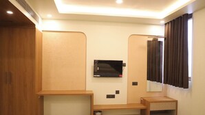A room with a television mounted on the wall, a wooden cabinet, a small shelf, and a trash bin.