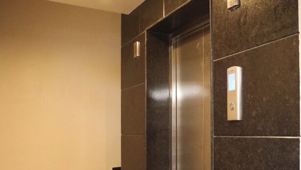 A modern elevator with a metallic finish, a wall-mounted light, and a set of black marble steps leading to it.