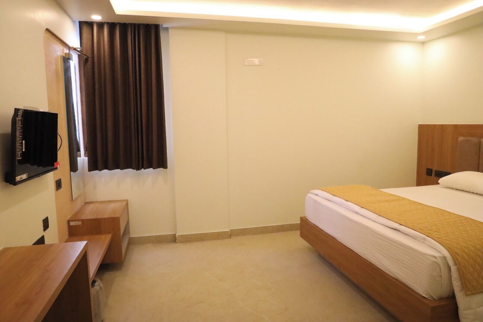 Ein Hotelzimmer mit einem Bett, einem Schreibtisch, einem Fernseher und einem Vorhangfenster.