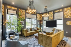 A modern living room with a sofa, armchairs, and a coffee table. There are large windows with blinds, a television, and decorative wall art. - East Nashville 4-Home Buyout With Rooftop, Sleeps 33 (Nashville)