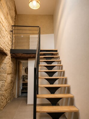 A staircase with wooden steps and a metal railing, leading to a landing with a light fixture above. - Stone house with a pool just outside Uzès (Garrigues-Sainte-Eulalie)