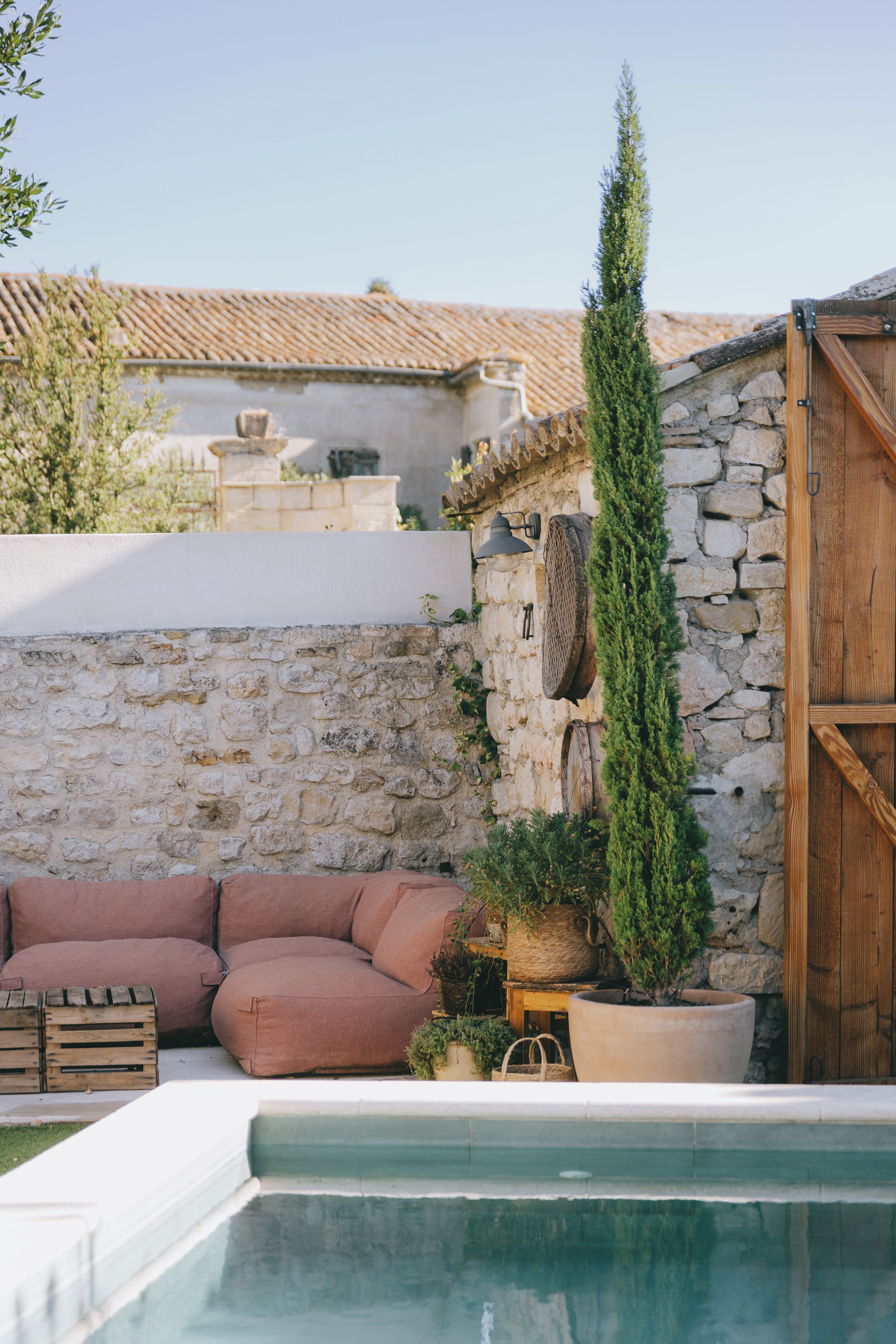 A pool area with a stone wall, a wooden door, and a seating area with cushions.