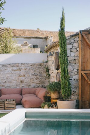 Un espace piscine agrémenté d’un mur en pierre, d’une porte en bois et d’un coin salon avec des coussins.