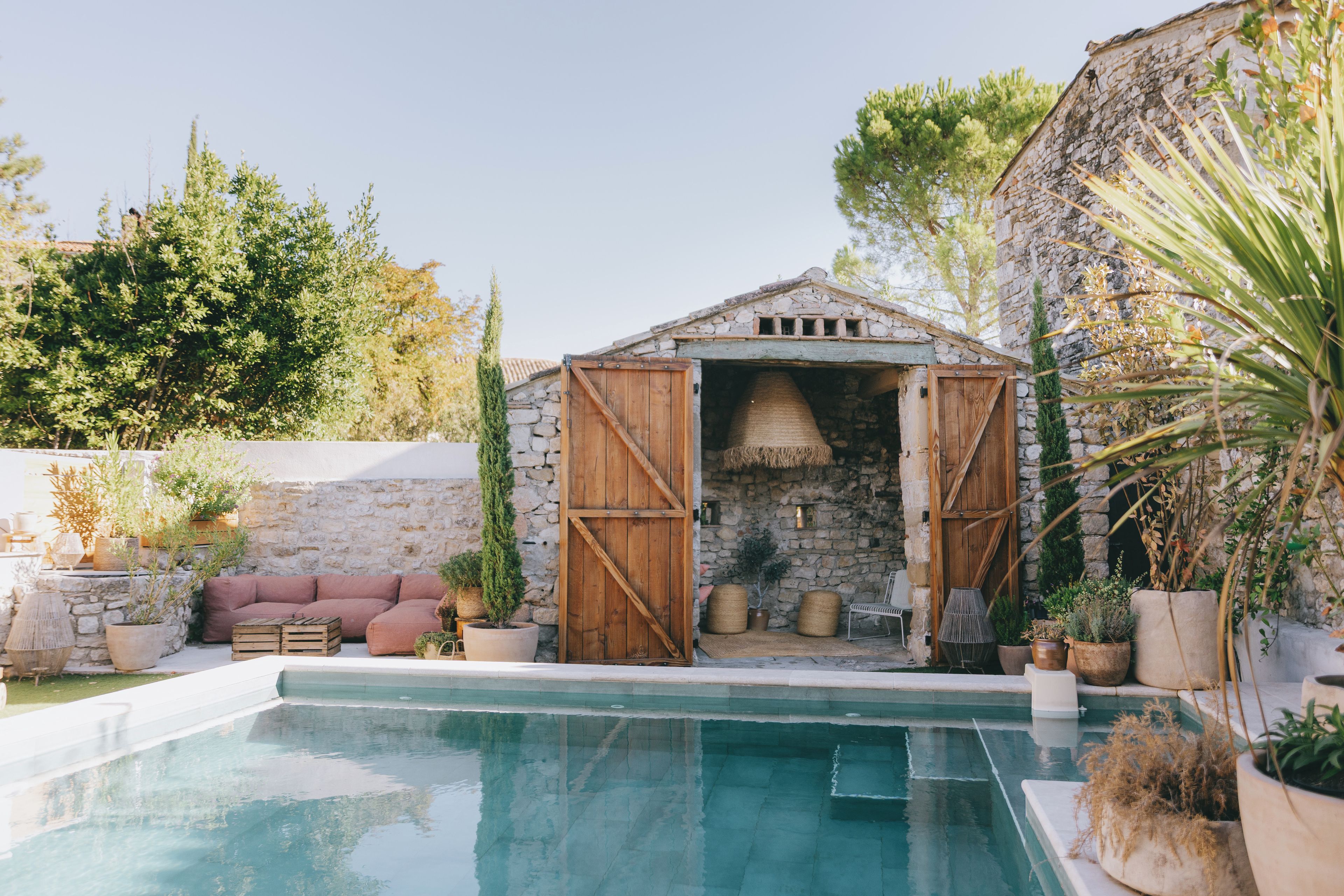 A pool area with a stone building, wooden doors, and outdoor seating.