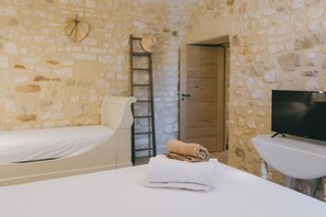 Quarto com parede de pedra, uma cama, uma televisão e uma toalha sobre uma mesa.