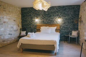 A bedroom with a stone wall, a bed with white bedding, two wall-mounted lights, and a wooden headboard. - Stone house with a pool just outside Uzès (Garrigues-Sainte-Eulalie)