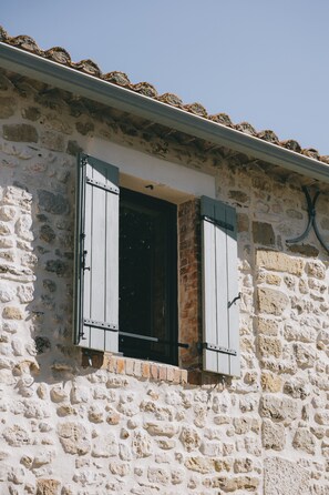 A stone building with a window featuring white shutters and a small balcony. - Stone house with a pool just outside Uzès (Garrigues-Sainte-Eulalie)
