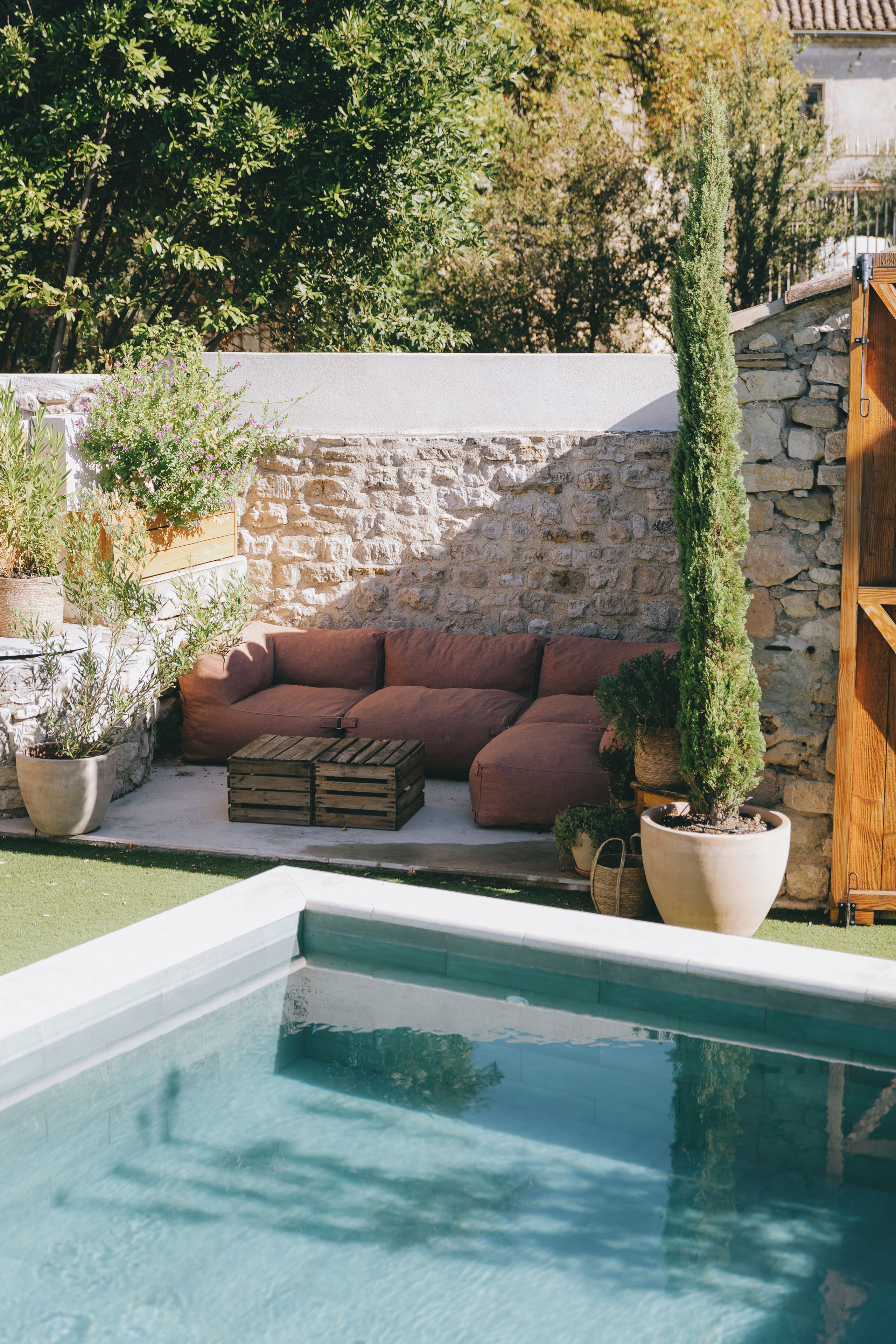 Un espace aménagé au bord de la piscine, avec un mur en pierre, un banc en bois et des plantes en pot.