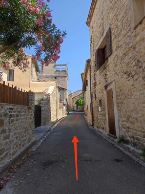 A narrow street with stone buildings on either side, a clear sky, and an arrow on the road indicating direction. - Stone house with a pool just outside Uzès (Garrigues-Sainte-Eulalie)